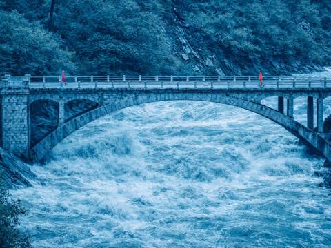 Architecture of Trust 1 – Zwei Personen gehen auf einer Brücken aufeinander zu, die über einen reißenden Fluss führt.