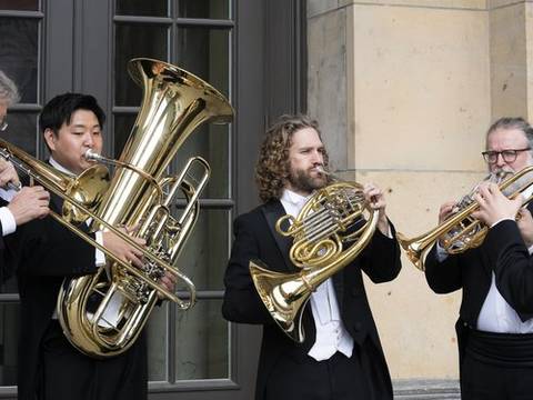 Konzerthaus Brass Berlin – Fünf Personen in schwarzen Anzügen und Fliegen spielen Blechblasinstrumente vor einem Gebäude mit Steinfassade und großen Fenstern.