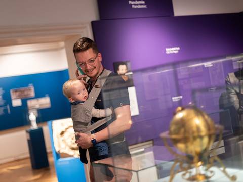 Mit dem Baby ins Museum bei der Elternzeit Kultur im Museum Ephraim-Palais. – Ein Mann mit Baby im Tragetuch und einem Audioguide am Ohr in der Ausstellung BerlinZEIT