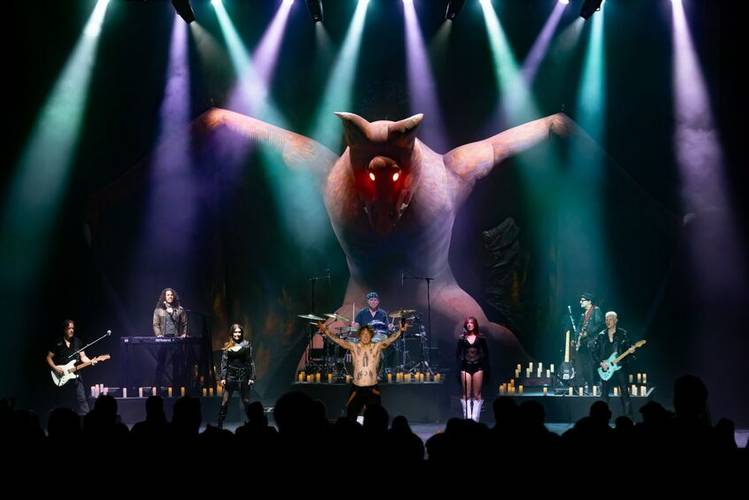 Bühne mit Band; riesige Fledermausfigur mit leuchtenden roten Augen im Hintergrund. Mehrfarbiges Scheinwerferlicht, viele Kerzen auf der Bühne.