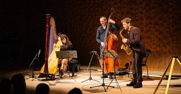 Kathrin Pechlof Trio – Drei Personen musizieren: eine Harfe spielende Person, eine person mit Kontrabass, eine Person mit Saxophon auf einer Bühne. Notenständer davor.