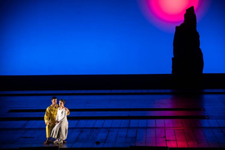 Die Zauberflöte – Zwei Personen auf einer Bühne, blaue Hintergrundbeleuchtung, pinke Sonne und schwarze Silhouette eines Felsens rechts.