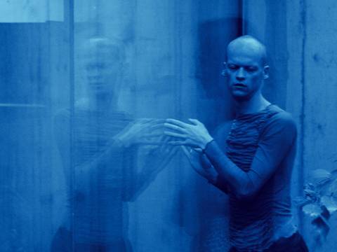 Sasha Waltz & Guests – Person bewegt die Hände vor einer spiegelnden Fläche; das Bild ist blau eingefärbt und zeigt eine verschwommene Spiegelung.