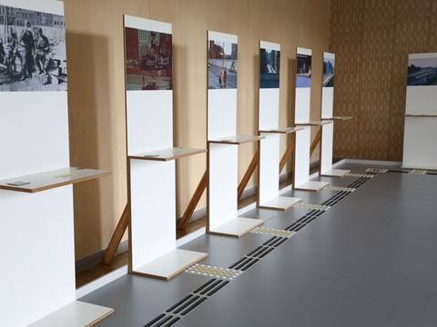 Blick in die Ausstellung "Sprechende Bilder" – Sieben Fotokonsolen mit Fotografien, am Boden das taktile Leitsystem