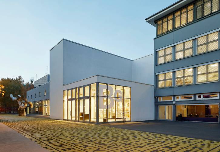 Berlinische Galerie, Außenansicht – Foto: Gebäude mit Flachdach und Glasfront, auf der das Logo der Berlinischen Galerie abgebildet ist. Davor ein Platz mit einer Metallskulptur und Bodenkunstwerk.