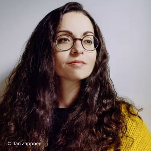 Marina Chernivsky – Eine Person mit langen, lockigen Haaren und Brille trägt einen gelben Pullover. © Jan Zappner.