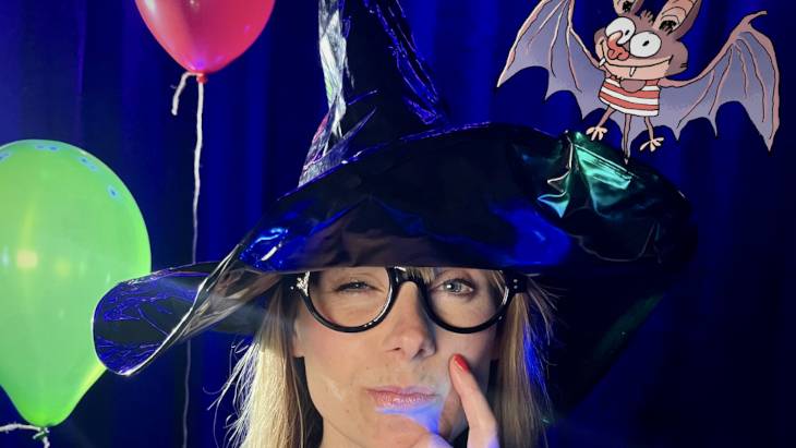Das Grusical – Person mit schwarzem Hexenhut und Brille, denkt nach. Roter und gruener Ballon im Hintergrund. Zeichentrickfledermaus in Streifen-Shirt oben rechts.