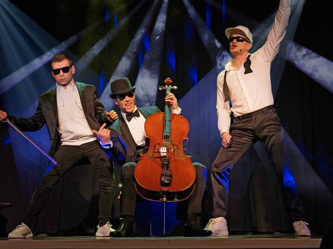 BEATHOVEN – Beat für Elise – Drei Personen mit Anzug und Sonnenbrille auf der Bühne; eine mit Cello in der Mitte, die anderen posieren seitlich mit Gesten.