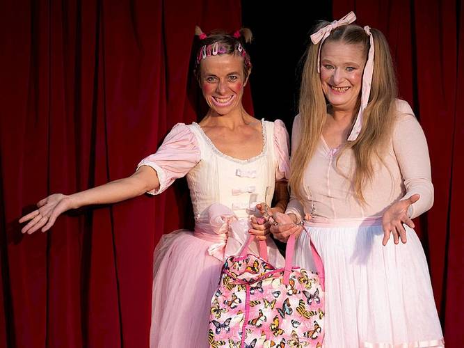 Märchen im Glaspalast von und mit dem Hexenberg Ensemble: Dornröschen | Hase und Igel – Zwei lachende Personen in rosa Ballettkostümen und Tüllröcken vor rotem Vorhang; sie halten eine pinke Tasche mit Schmetterlingen.