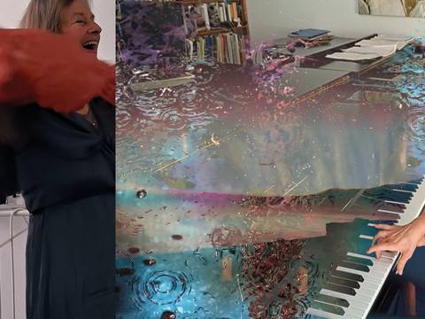  – Person in blauem Kleid hebt orange Stoff; daneben Hände auf Klavier mit buntem, wasserartigem Effekt; im Hintergrund Bücherregal und Kunst.