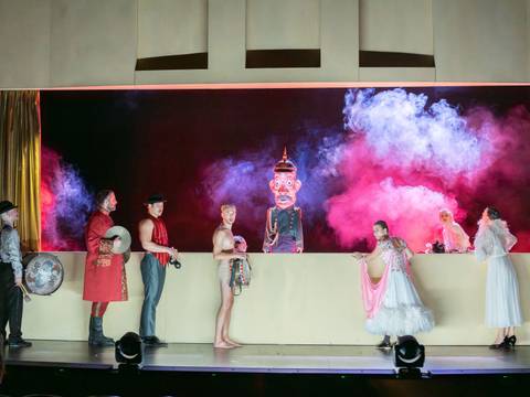 Der Hauptmann von Köpenick – Männer und Frauen mit Instrumenten stehen vor einer Art Kasperletheater mit einer uniformierten Figur mit Pappmachékopf