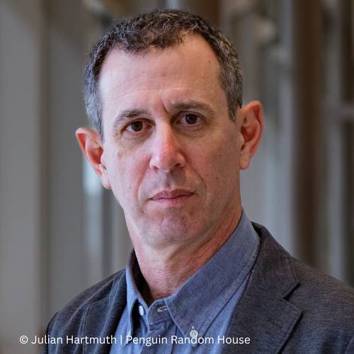 Assaf Gavron – Männlich gelesene Person mit kurzem Haar, grauer Jacke und blauem Hemd vor unscharfem Hintergrund. Text: © Julian Hartmuth Penguin Random House.