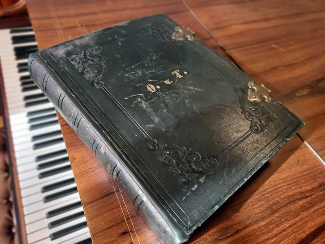 Leder-Einband des Portrait-Albums mit goldgefassten Initialen O. v. T. (Ottilie von Thile) und Messing-Verschlüssen. – Ledergebundenes Album auf Konzertflügel