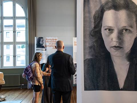 Blick in die Ausstellung "Lang ist es nicht her. Und jetzt ist es soweit." – Ein Panel mit Portraitaufnahme der Schriftstellerin Susanne Kerckhoff, im Hintergrund Besuchende in der Ausstellung.