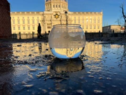 Hauptbild für die Veranstaltung "Über Wasser… aus der Pfütze" – Schale mit Wasser in einer Pfütze vor dem Humboldt Forum