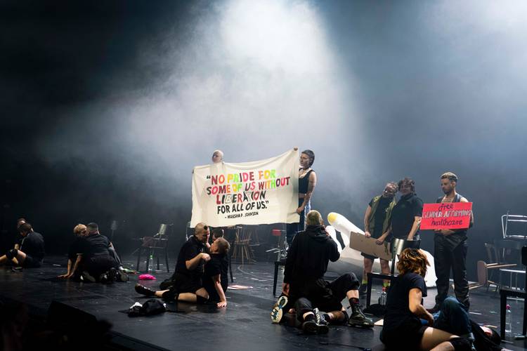 Personen auf einer Bühne halten Banner mit den Texten: "NO PRIDE FOR SOME OF US WITHOUT LIBERATION FOR ALL OF US" und "Free gender affirming healthcare".