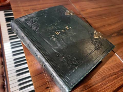 Leder-Einband des Portrait-Albums mit goldgefassten Initialen O. v. T. (Ottilie von Thile) und Messing-Verschlüssen. – Ledergebundenes Album auf Konzertflügel