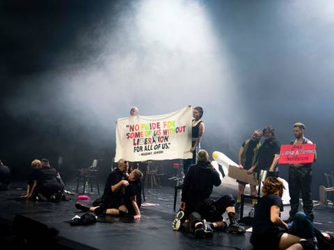  – Personen auf einer Bühne halten Banner mit den Texten: "NO PRIDE FOR SOME OF US WITHOUT LIBERATION FOR ALL OF US" und "Free gender affirming healthcare".