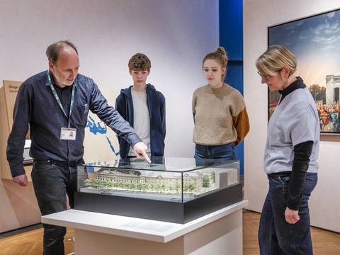  – Ein Museumsführer steht vor einem Modell des Zeughauses und erklärt es drei Personen.