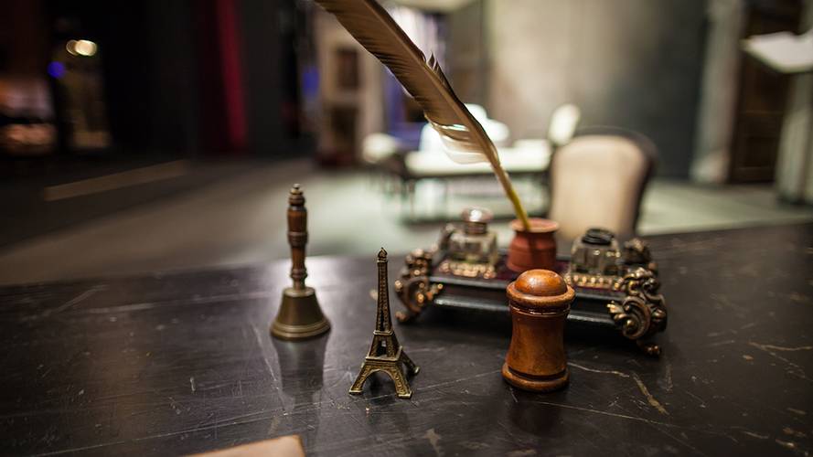 Backstage-Führung – Eine Feder steht in Tinte auf einem dekorativen Holzstift, daneben Eiffelturm-Miniatur und zwei Briefbeschwerer auf einem alten Schreibtisch.