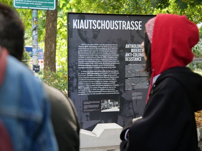 Die „Kiautschoustraße“ wurde 1905 nach der deutschen Kolonie Jiāozhōu an der chinesischen Ostküste benannt. Die Gedenkstele erklärt den kolonialen Kontext des Straßennamens und ergänzt ihn um antikoloniale Gegenerzählungen. – Gedenkstele an der Kiautschoustraße, die den kolonialen Kontext des Straßennamens erklärt und ihn um antikoloniale Gegenerzählungen ergänzt
