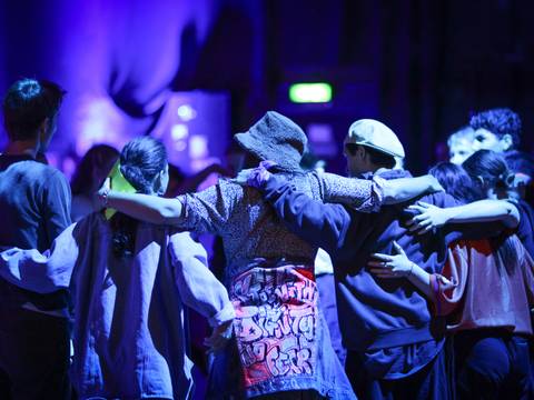 Arena #4 (Dance Battle) – Junge Tänzer*innen in einer Umarmung im großen Kreis. Von hinten fotografiert in violetter Lichtstimmung.