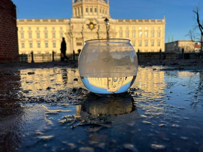 Hauptbild für die Veranstaltung "Über Wasser… aus der Pfütze" – Schale mit Wasser in einer Pfütze vor dem Humboldt Forum