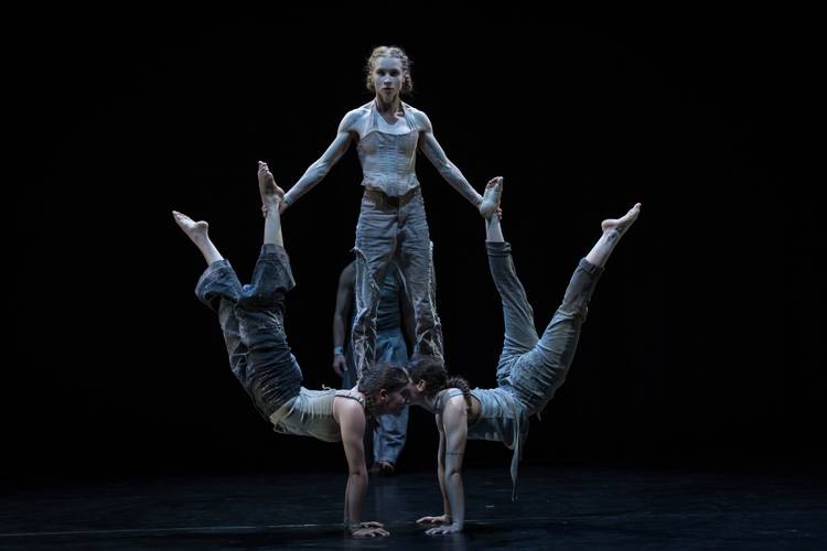 North of Now – Zwei Künstler*innen machen einen Handstand mit den Köpfen zusammen und beugen sich ab der Hüfte aufwärts. Auf ihren Schultern steht eine weitere Künstlerin und hält die Füße.