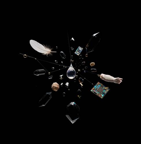 Kristalle, Feder, Wassertropfen, mehrere Glühbirnen, Computerchip und gemalte Hand vor schwarzem Hintergrund, radial angeordnet.