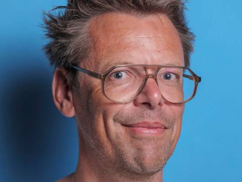 Markus Köhle – Person mit Brille und hellem T-Shirt vor hellblauem Hintergrund. Kurze zerzauste Haare, leichtes Lächeln, Blick direkt zur Kamera.