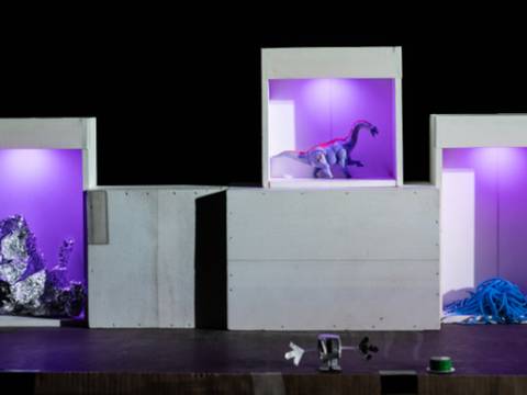 Der Viereckplanet – Drei beleuchtete Boxen mit violettem Licht. Links Alufolie, Mitte Dinosaurierfigur, rechts blaue Schnur. Unter den Boxen sind kleine Gegenstaende.