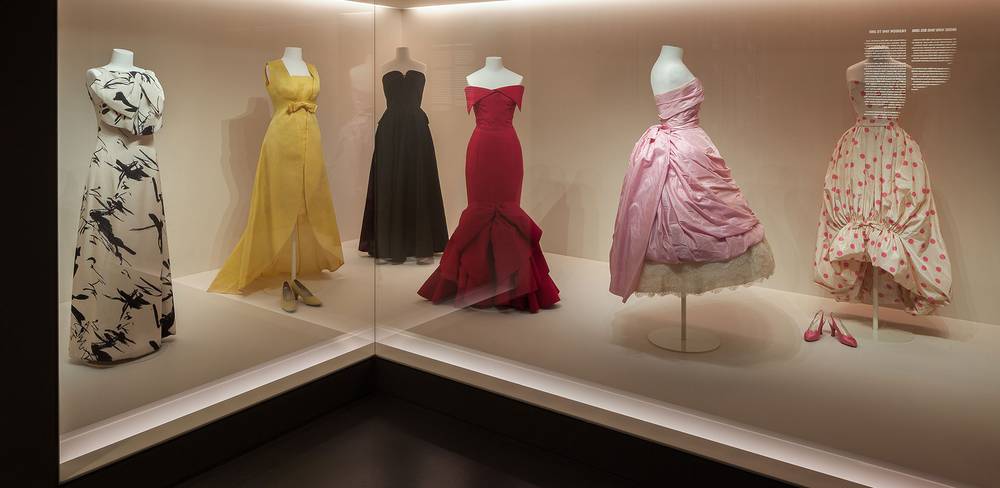 Kleider der 1960er-Jahre von Jean Patou, Christóbal Balenciaga und Jean Dessès in der Modegalerie des Kunstgewerbemuseums – Sechs Schneiderpuppen in einer beleuchteten Glasvitrine mit eleganten Abendkleidern in verschiedenen Farben und Designs, von links nach rechts: schwarz-weiß