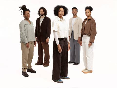 Neneh Boye & Band – Fünf Personen stehen nebeneinander auf weißem Hintergrund. Alle tragen lässige Anzüge und Hemden.