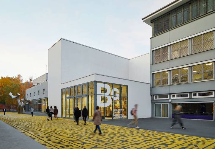 Berlinische Galerie, Außenansicht – Moderne Gebäudefassade der Berlinischen Galerie mit großen Fenstern und Beschriftung. Vorplatz mit gelbem Raster und Schrift. Menschen spazieren.