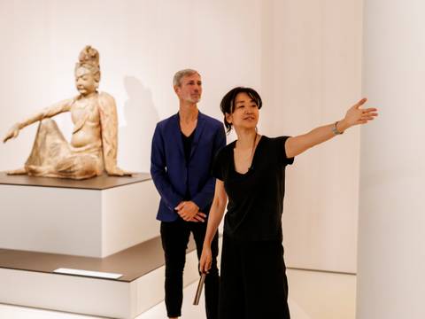 Führung Un-sichtbare Hände im Museum für Asiatische Kunst – Eine Frau erklärt eine Buddha-Statue in einem Kunstmuseum, während ein Mann interessiert zuhört.
