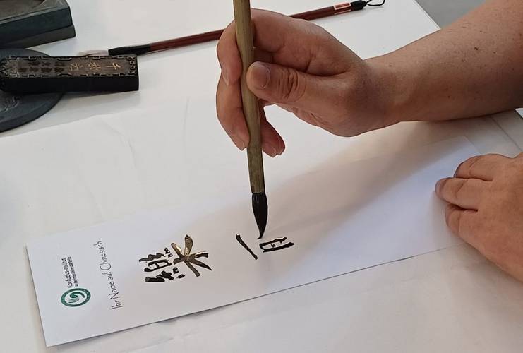 Teilnehmer:innen dieses Mitmach-Angebots können eine chinesische Kalligrafie ihres Namens mit nach Hause nehmen. – eine chinesische Kalligrafie entsteht