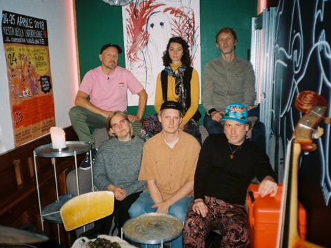 Ingebrigt Håker Flaten (Exit) Knarr – Eine Gruppe von Personen in einem Raum mit Postern und Kunst an der Wand, sitzend und stehend. Instrumenten nah.