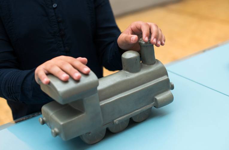 Die Form einer Lokomotive an einem Modell ertasten. – Hände ertasten das Modell einer Lokomotive.