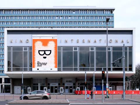 Fotografie „Kino International“, Karl-Marx-Allee, Berlin, 2022 Schriftzug: Klaus Wittkugel (1910–1985), 1961 Berlinale-Plakat: Claudia Schramke (*1985), 2022 – Außenansicht des Kino International in Berlin mit einem großen orange-weißen Berlinale-Plakat, das einen Bären mit Brille zeigt