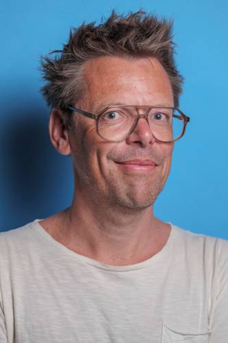 Markus Köhle – Person mit Brille und hellem T-Shirt vor hellblauem Hintergrund. Kurze zerzauste Haare, leichtes Lächeln, Blick direkt zur Kamera.