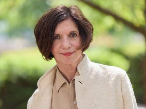 Prof. Dr. h.c. Jutta Allmendinger – Eine Person mit schulterlangem, glattem Haar, hellem Mantel und beigem Hemd steht draußen vor unscharfem, grünem Hintergrund.