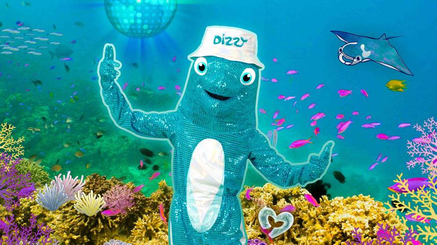 Ein blauer Fisch-Maskottchen mit Hut "Dizzy" unter Wasser, umgeben von Fischen, Korallen und einer lila Discokugel. Rechts ein Rochen.