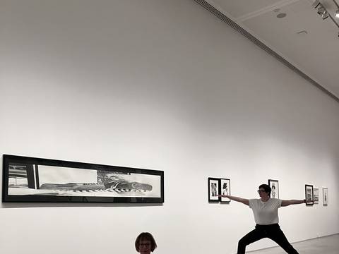 Yoga in der Ausstellung „Marc Brandenburg. 20th Century Debris“ – Foto: Zwei Personen in Yoga-Kleidung sitzen beziehungsweise stehen in unterschiedlichen Yoga-Posen im Ausstellungsraum.
