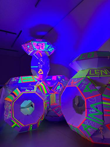 Drop-In HUFO UFO in den Werkräumen der Akademie – Leuchtende geometrische Skulpturen in einem dunklen Raum, umgeben von bunten Neonfarben und Mustern