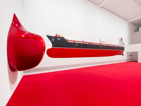 Ausstellungsansicht „Monira Al Qadiri. Hero“ – Foto: Blick in den Ausstellungsraum der Ausstellung von Monira Al Qadiri, der eine große rot-schimmernde Skulptur an der Wand und einen langen Öltanker zeigt, der auf die Wand aufgemalt wurde.