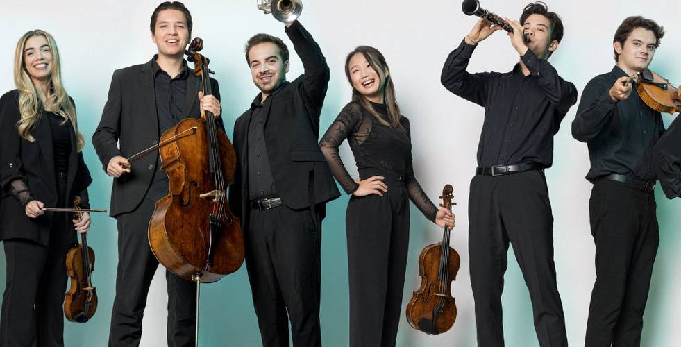 Fünf Personen mit Musikinstrumenten: zwei Geigen, ein Cello, eine Trompete, eine Klarinette. Alle tragen schwarze Kleidung und lächeln.