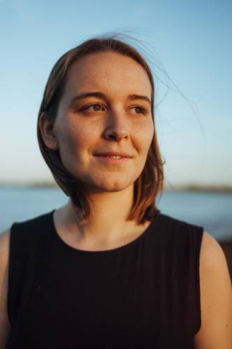 Porträt der Slam-Poetin Mona Harry – Porträt einer Frau mit kurzen Haaren, die am Wasser steht, bei Sonnenuntergang, mit einem sanften Lächeln und natürlichem Licht.