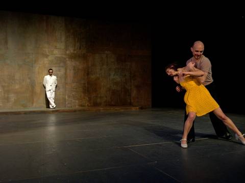 Zweiland 1 – Im Vordergrund ein Paar, das tanzt. Im Hintergrund eine Person in weißem Anzug, die an der Wand lehnt.