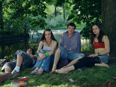 Rineke Dijkstra, Vondelpark, June 10, 2005 – Fotografie: Vier junge Personen sitzen bzw. liegen in Sommerkleidung in einem Park. Ihr direkt ist direkt in die Kamera gerichtet.