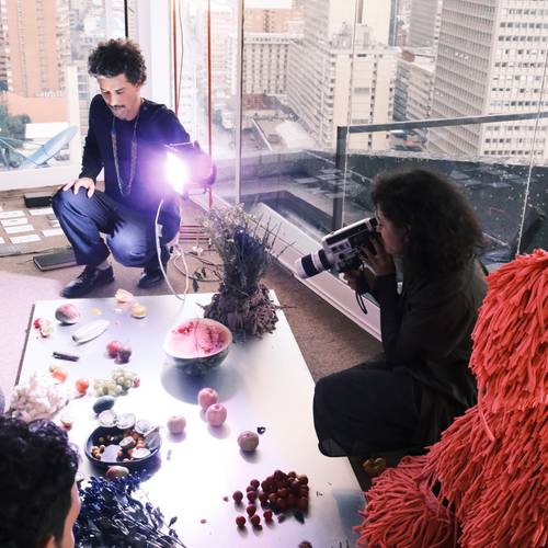 Embodied Practices – Talk über Körperwissen 3 – Zwei Personen dokumentieren eine Installation aus Früchten und Naturmaterialien in einem Innenraum mit Stadtblick.